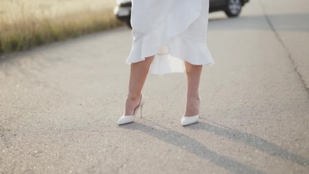 Jambes féminines en robe blanche et chaussures marche sur la route hors de la ville et marches élégantes — Video