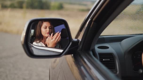 Αντανάκλαση της γυναίκας στο αυτοκίνητο καθρέφτη, οι οποίοι εφαρμόζουν lip gloss και χαμογελώντας — Αρχείο Βίντεο
