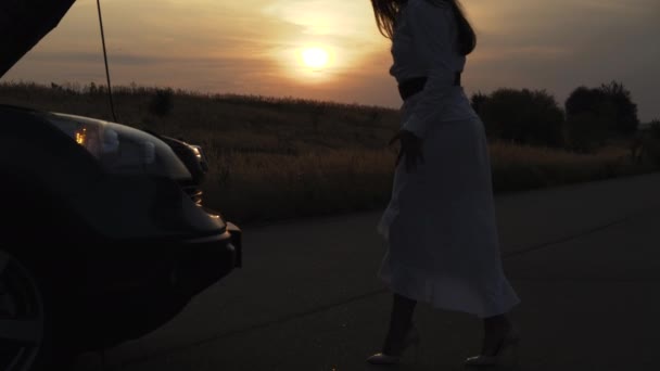Вид обеспокоенной женщины шагает к сломанной машине и приседает у нее глубоким вечером — стоковое видео