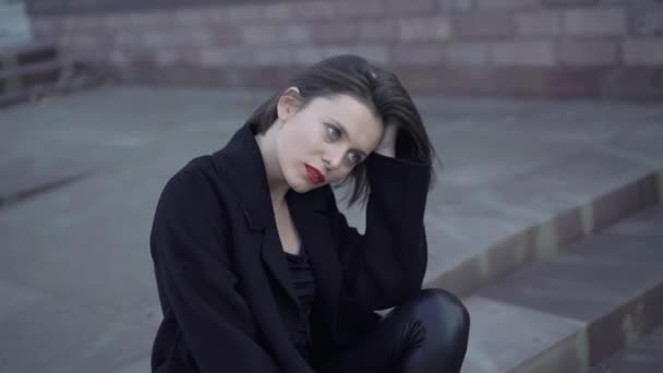 Portrait de dame réfléchie assise sur les escaliers de la rue et regarde de côté