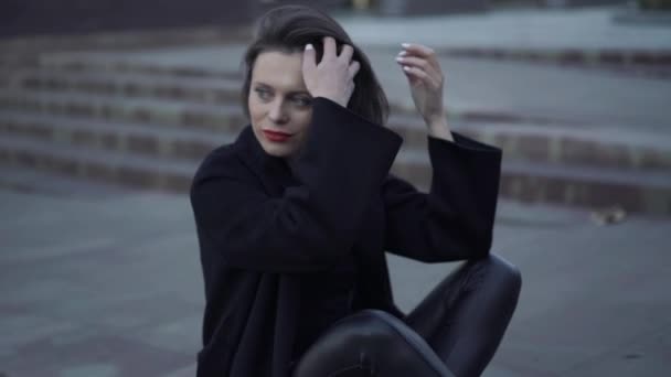 Стильная модель с красными губами и черной одеждой позирует на лестнице — стоковое видео
