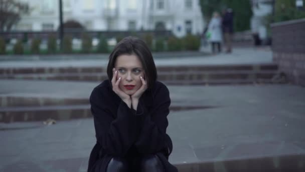 Portrait of mused woman sitting on street stairs and leaning her head on hands — Stock Video