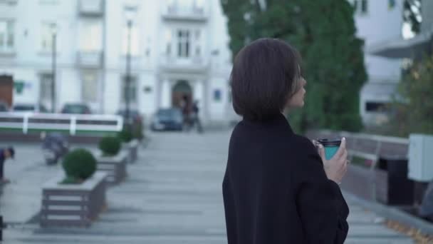 Уверенная леди с чашкой напитка в руке позирует перед камерой на улице — стоковое видео