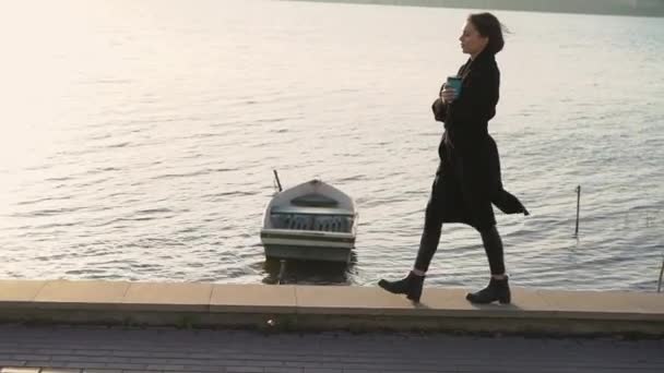 Dame met kopje drank wandelen op de grens bij het meer in winderige avond — Stockvideo