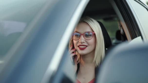 Щаслива бізнес-леді в окулярах розмовляє по телефону в машині і дивиться навколо — стокове відео