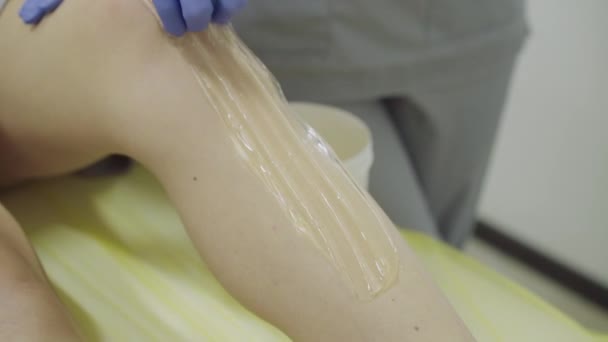 Aplicar uma pasta de açúcar e removê-lo da perna feminina no sofá — Vídeo de Stock