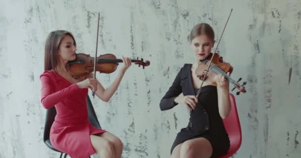 Dwie eleganckie dziewczyny w sukienkach grające na skrzypcach emocjonalnie na tle wnętrza — Wideo stockowe
