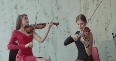 İçeride keman çalan elbiseli bayan müzisyenlerin düeti.