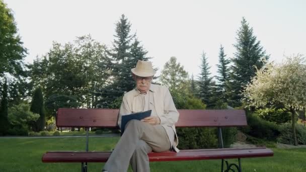 Tyylikäs vanhempi mies istuu puistonpenkillä ja kirjoittaa papereita — kuvapankkivideo