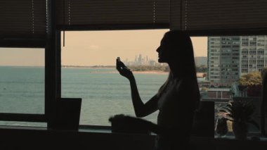 Güzel bir genç kadının silueti aynanın önünde makyaj fırçasıyla toz sürüyor, güzellik. Arkasında okyanus olan bir şehir..