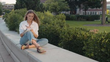 Çekici bir kadın deftere not alıyor dışarıda tek başına oturuyor. Gülümseyen akıllı kız parkta günlüğe düşünceler yazıyor. Kendine güvenen yazar kadın dışarıda kağıt not defteri tutuyor. Yavaş çekim