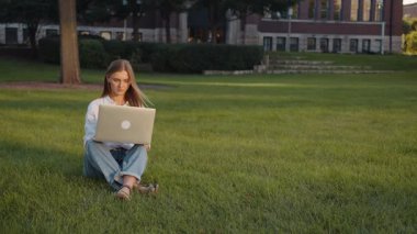 İş kadını, iş kadını, kız öğrenci, iş kadını, dizüstü bilgisayarda, internette, açık havada, sosyal ağlara göz gezdirmekle meşgul. Odaklanmış kadın çimenlerde oturuyor..