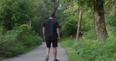 Yeşil bahar ormanlarında bir adam yolda yürüyor, tek ayağı üzerinde topallayarak, 4k