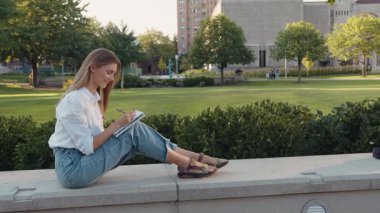 Gülümseyen kadın şehir bölgesinde elinde kalemle günlük tutuyor. Fotokopi kitabında kompozisyon hazırlayan çekici bir kız. Açık havada defter ile ders çalışan yetenekli bir genç. Ev ödevi yapan kız öğrenci.