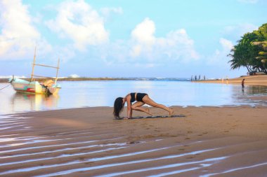 Şafakta sahilde yoga yapan bir kadın.