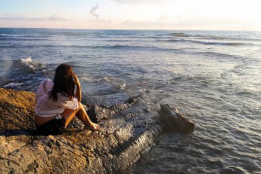 Kız geri döndü oturur ve kayalar üzerinde denize bakar