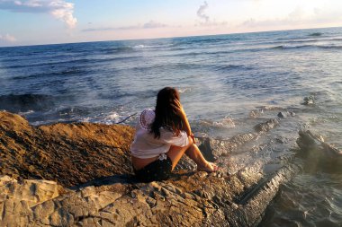 Kız geri döndü oturur ve kayalar üzerinde denize bakar