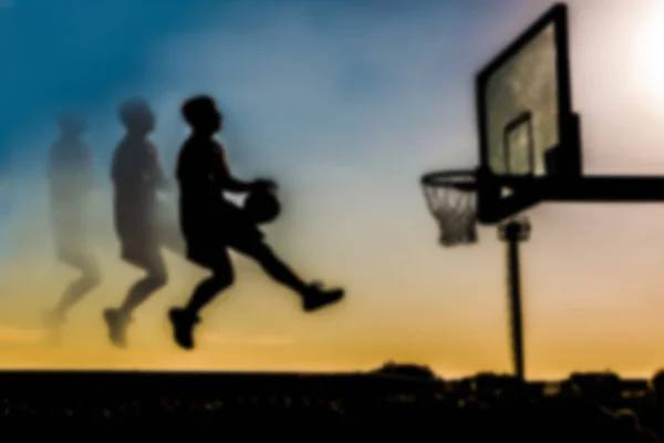 Blur or defocused silhouette of an unrecognizable basketball player in motion in flight with a ball on a sunset background in the direction of the ring