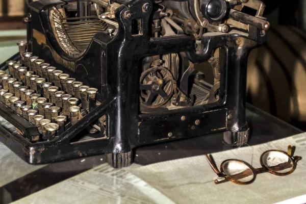 antique black typewriter near to old newspapers and glasses