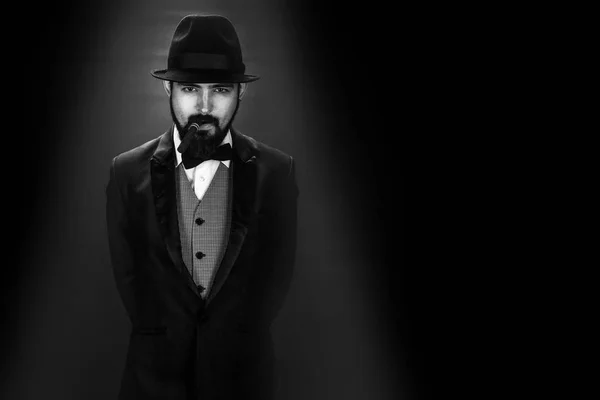 black and white portrait of bearded smoking gentleman in a suit with a butterfly and black hat