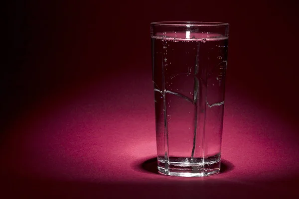 transparent glass with mineral water on a red background with space for text