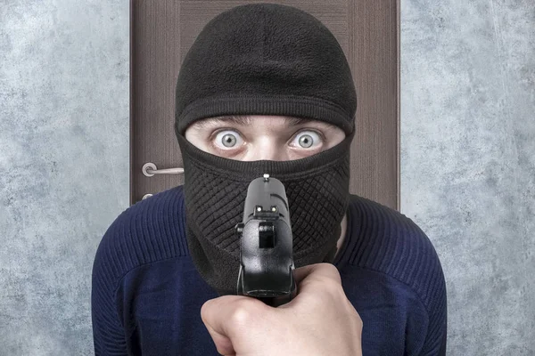 gun aimed at the criminal in balaclava, the image on the background of the door, the concept of catching the thief