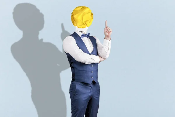 a man on blue background in a suit with a light bulb of crumpled yellow paper instead of a head with a raised finger, the concept of the idea
