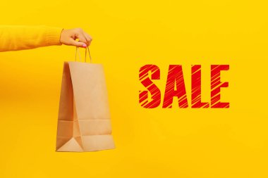 Sarı arka planda kağıt alışveriş torbası, indirimler ve satış konsepti