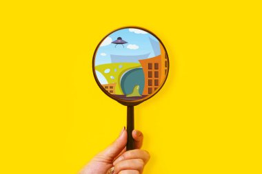 Magnifying glass over city with a UFO, alien creature search concept clipart