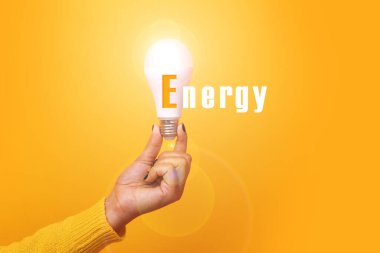 El ele tutuşan ampul, yazı enerjisi, aydınlatılmış ampul, sarı arkaplan üzerinde görüntü.