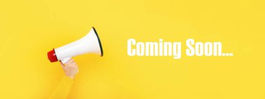 megaphone in hand and inscription coming soon on a yellow background clipart