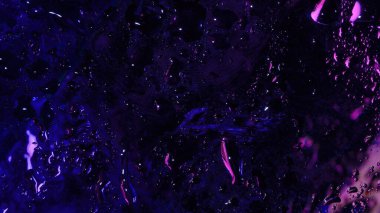 Dağınık su damlacıkları ve sıvı lekeleri içeren koyu mor ve mor neon ışık yansımaları olan soyut makro cam çekimleri..