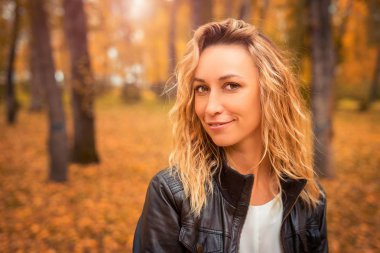 Kız sonbahar parkta yürüyor. Esmer ormandaki bir deri ceketli. Sarı yaprak Güz.