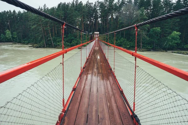 Suspension bridge on the river. Rainy weather, the road to the forest on the bridge over the river