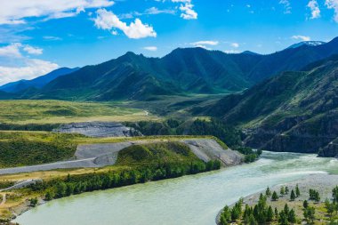 Dağ manzarası. Dağ ve vadi, yeşil çim ve fırtınalı dağ nehir, parlak gökyüzü ve bulutlar.
