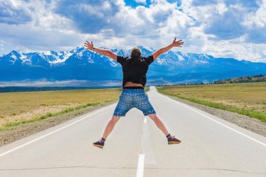 Bir adam yolda atlar. Dağların önünde karayolu üzerinde adam atlar. Dağların yüksek karlı zirveleri.