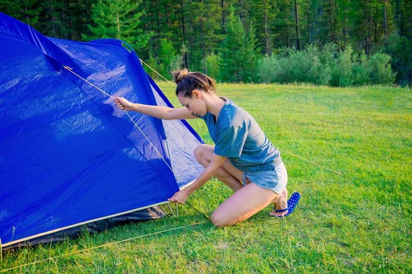 The girl sets up a tent on the grass. Tourist fortifies the tent, camping