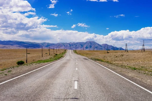 Highway from the desert to the mountains. Empty straight road leaving into the distance. Mountain landscape.