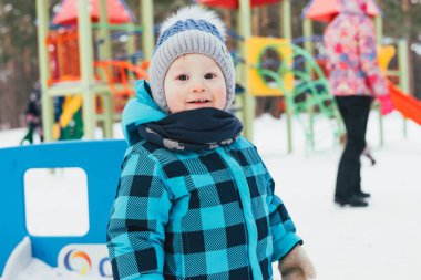 Bir çocuk oyun kış elbiseli. Kış yürüyüş parkı, şapka, eşarp, sıcak ceket. Kar, kırmızı yanakları, yüzünde gülümseme.