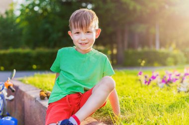 Çocuk palyaçoluk ve pozlar oturur. Bir preschooler portresi. Akşam güneş ışınlarının bir yatakta bir parkta çocuk oturur.