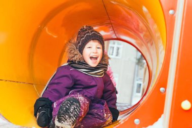 Çocuk parkta kışın çalış. Neşeli bebek oyun oynuyor. Atkı, şapka, eldiven,