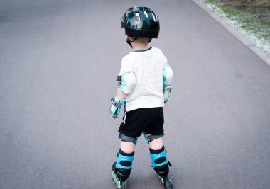 Koruyucu kask takan küçük bir çocuk paten sürüyor..