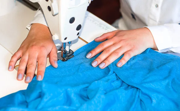Terzi. Bir kadın dikiş makinesine mavi kumaş karalıyor..