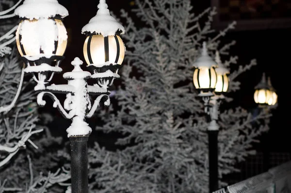 Vintage street lights lit on the streets of the city at night. Winter city landscape. Snow-covered fence and lamps.