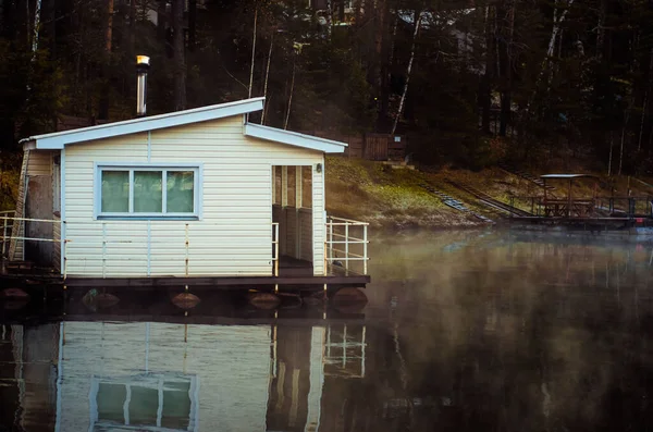 Sudaki beyaz ev. Bina cambaz ayaklıklarının üzerinde gölette duruyor. Dağların arasındaki gölün üzerinde hafif bir sis.