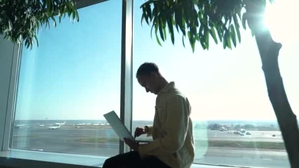 Молодой человек работает на ноутбуке в аэропорту — стоковое видео