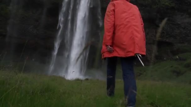 Отслеживание снимка женщины, валяющейся в Исландии над Скогафоссом — стоковое видео