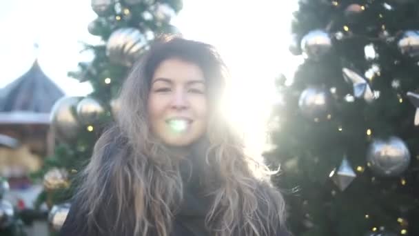 Gyönyörű fiatal nő, vonzó mosolyt portréja. Csinos lány, a hosszú haj látszó fényképezőgép és mosolyogva a karácsonyfa háttér.. — Stock videók