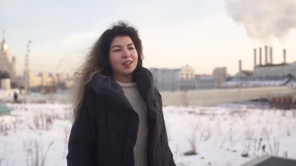 Молодая женщина стоит на фоне труб металлургического завода в зимний день . — стоковое видео