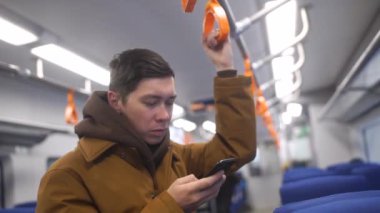 Toplu taşıma yakışıklı adam ayakta görünümünü kapatın. Kalabalık tramvay iç. Cep telefonuna türlerine açık. Lüks kol saati. Casual giyim.
